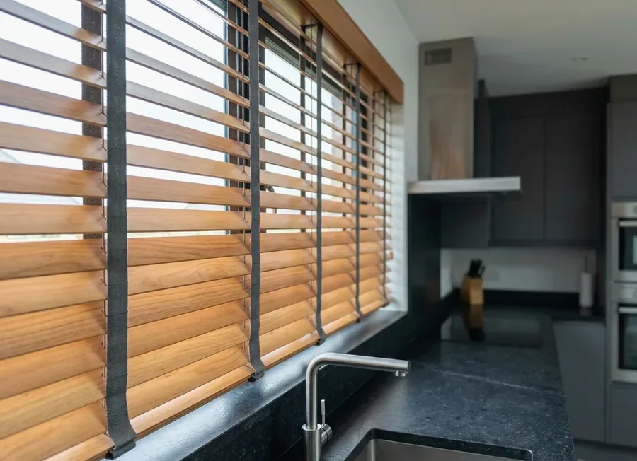 Timber venetian blind above a kitchen counter in a Blair Atholl home, warm wooden slats carried on charcoal fabric tapes